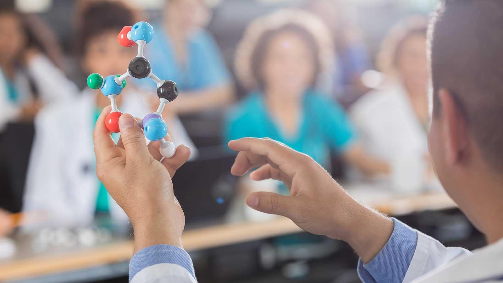 Person holding plastic molecule bonds representing Biology program at Clarkson